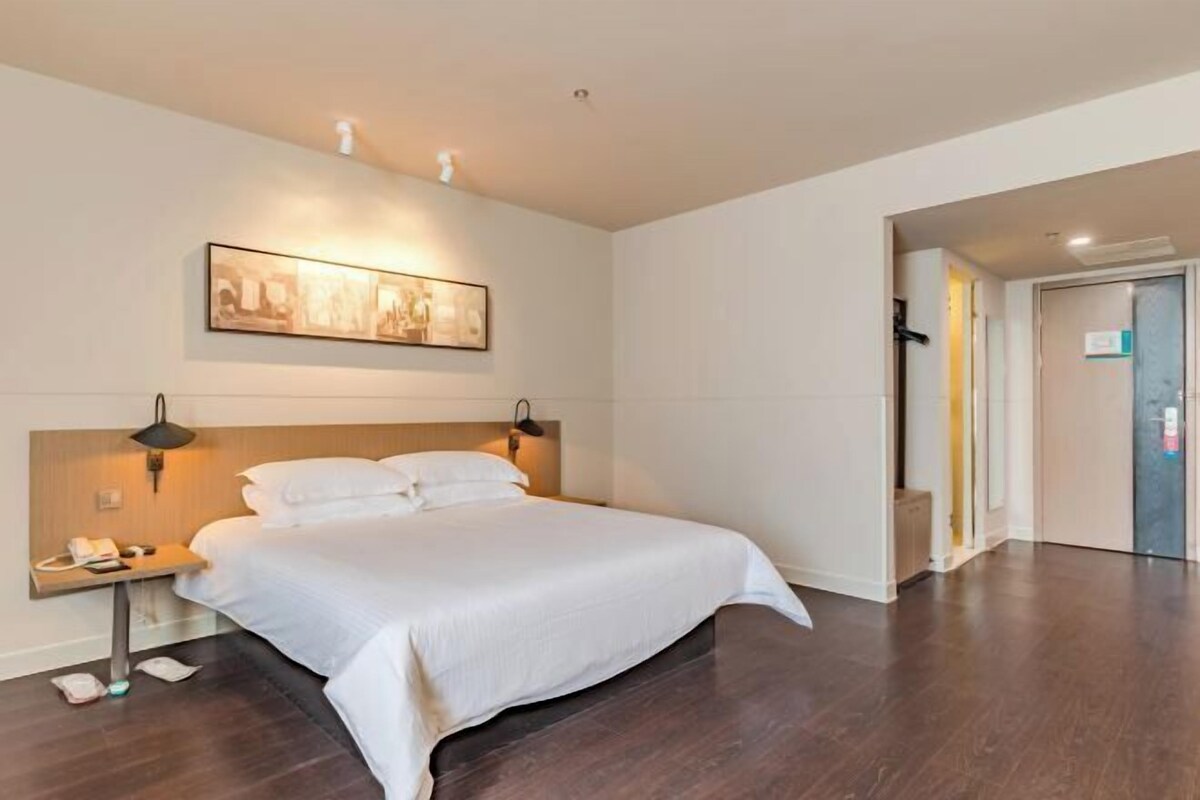 A modern hotel room with a large bed, a bedside table with a lamp, and a framed artwork on the wall.