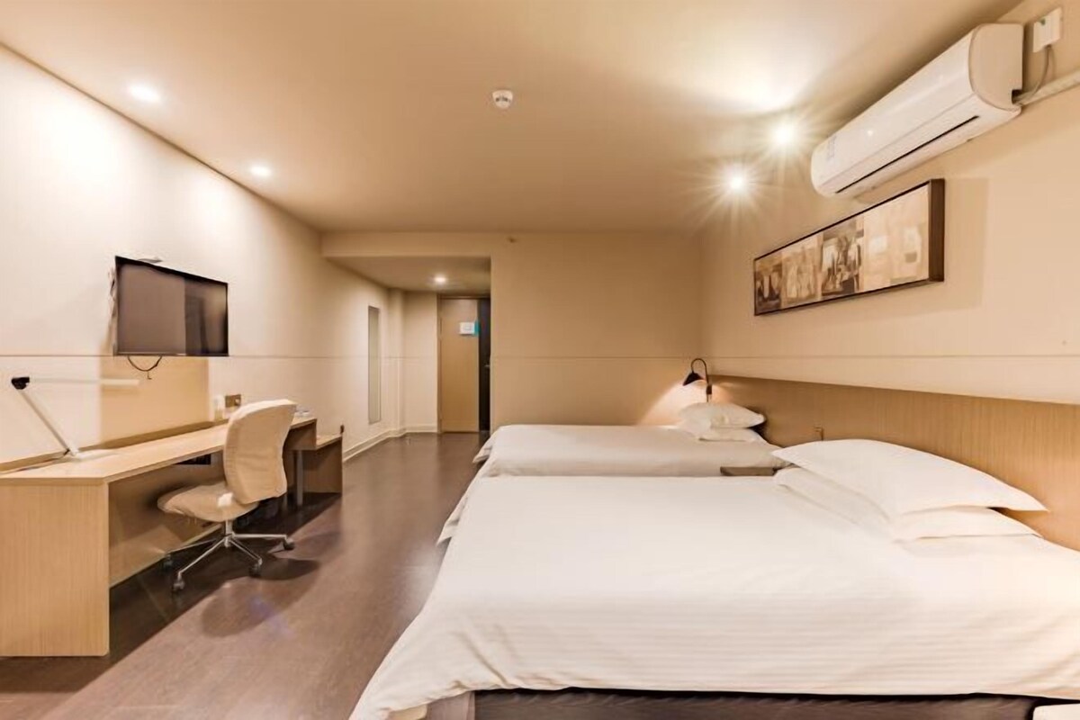 A hotel room with a desk, chair, two beds, and a mounted TV.