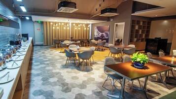 A modern hotel lobby with a long reception desk, seating area, and a television screen.