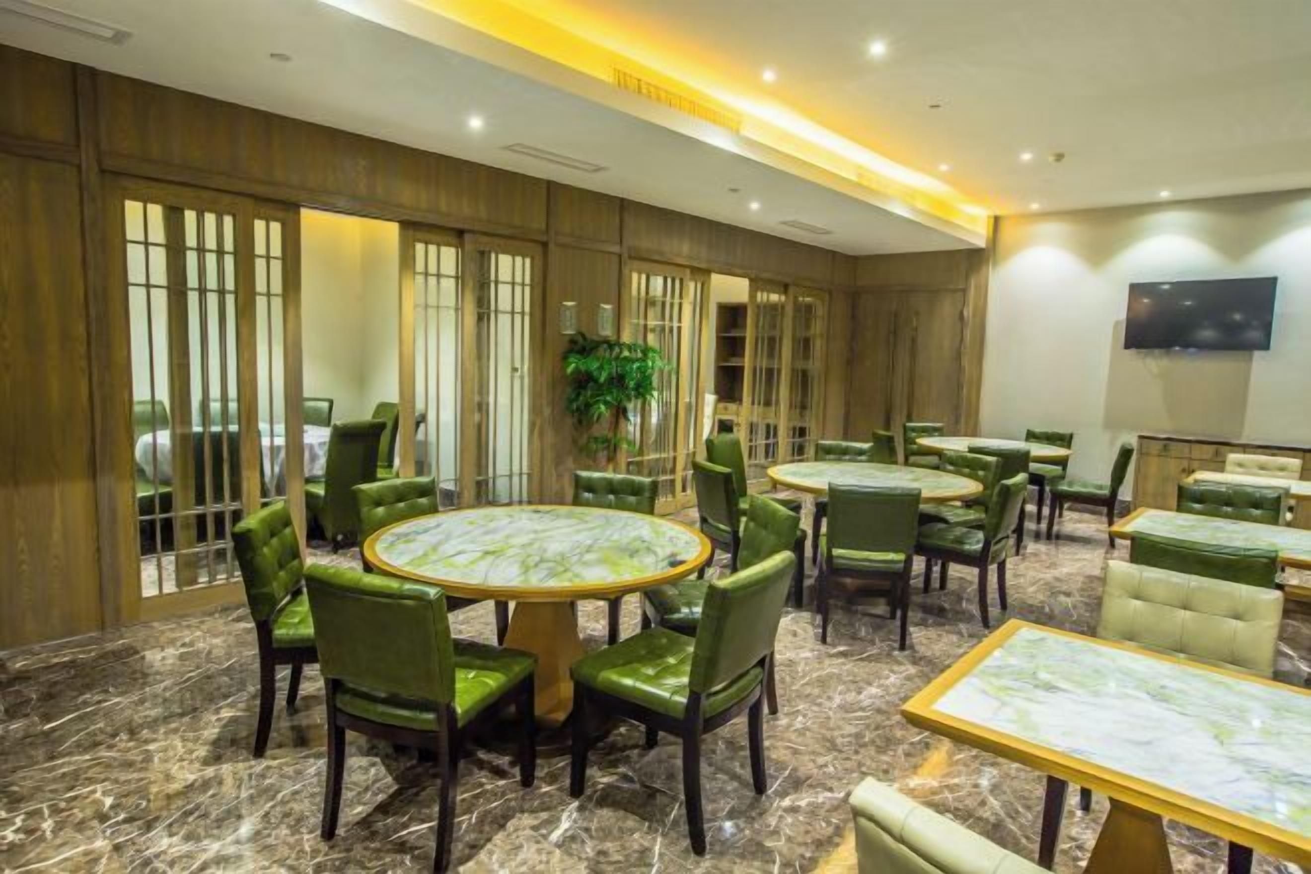 Un salón de conferencias de hotel con mesas redondas, sillas tapizadas en verde y una planta grande en maceta.