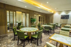 Une salle de conférence d’hôtel avec des tables rondes, des chaises recouvertes d’un tissu vert et une grande plante en pot.