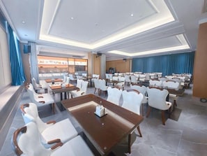 A spacious hotel dining area with multiple tables and chairs, a large window with curtains, and a view of the city. - Vienna Hotels Group Zhuhai (Zhuhai)