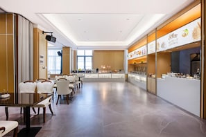 A modern dining area with a long counter, multiple seating options, and a variety of food display cases. - Vienna Hotels Group Zhuhai (Zhuhai)