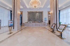 A spacious lobby with a marble floor, a grand chandelier, and a reception desk with framed certificates. - Vienna Hotels Group Zhuhai (Zhuhai)
