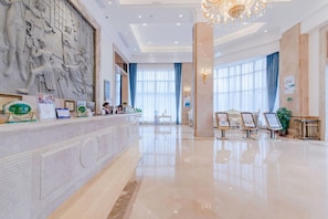 A hotel lobby with marble flooring, a reception desk, a large wall sculpture, and a chandelier. - Vienna Hotels Group Zhuhai (Zhuhai)