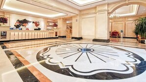 A spacious lobby with a large marble floor, a reception desk, and a chandelier.