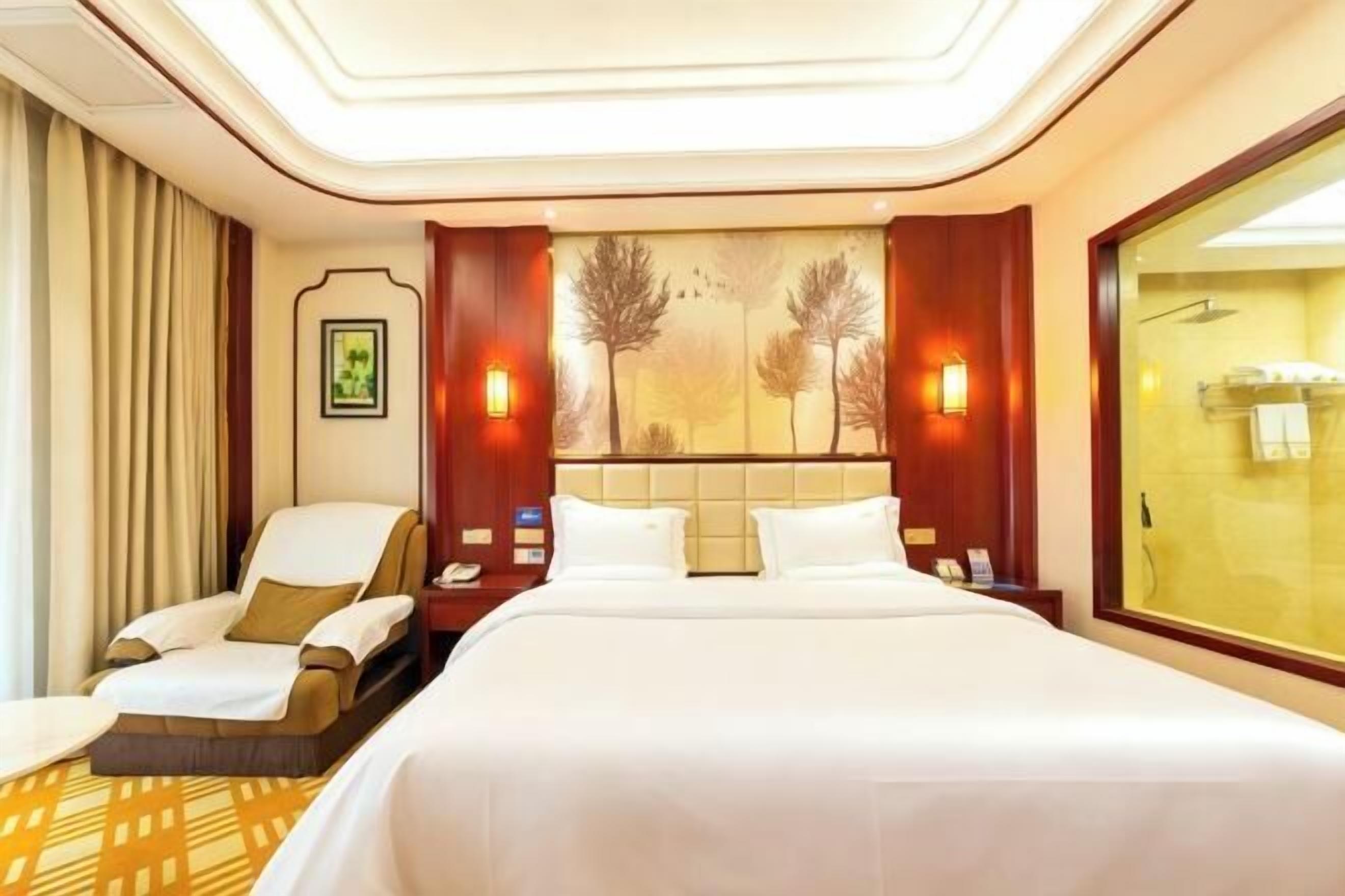 A hotel room with a large bed, a chair, a nightstand, and a window.