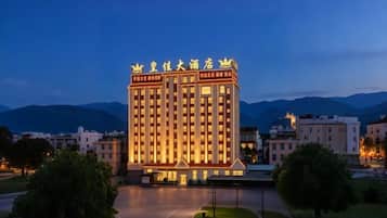 Un hotel de varios pisos con una entrada destacada, rodeado de vegetación y con montañas al fondo.