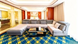 A modern hotel room with a large L-shaped gray sofa, a small coffee table, and a patterned carpet.