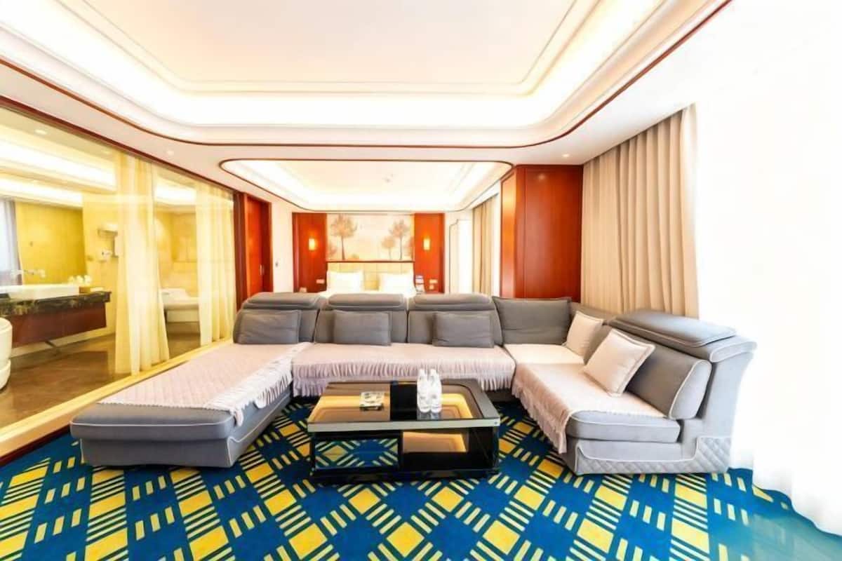Moderni hotellihuone, jossa on suuri, L-muotoinen harmaa sohva, pieni sohvapöytä ja kuviollinen matto.
