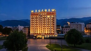 A multi-story hotel with a prominent entrance, surrounded by greenery and mountains in the background.