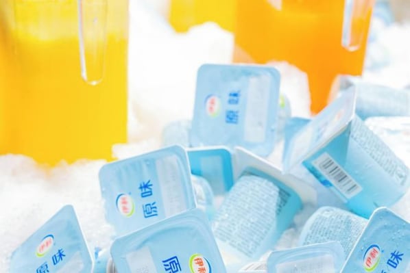A collection of blue containers with Chinese characters, possibly dairy products, on a surface with a yellow liquid in the background.