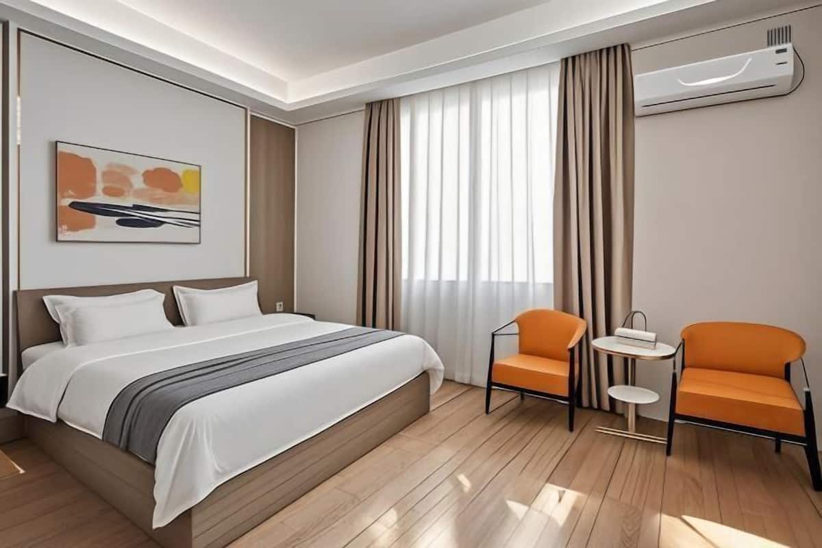 A hotel room with a bed, two chairs, a small table, and a wall-mounted air conditioner.