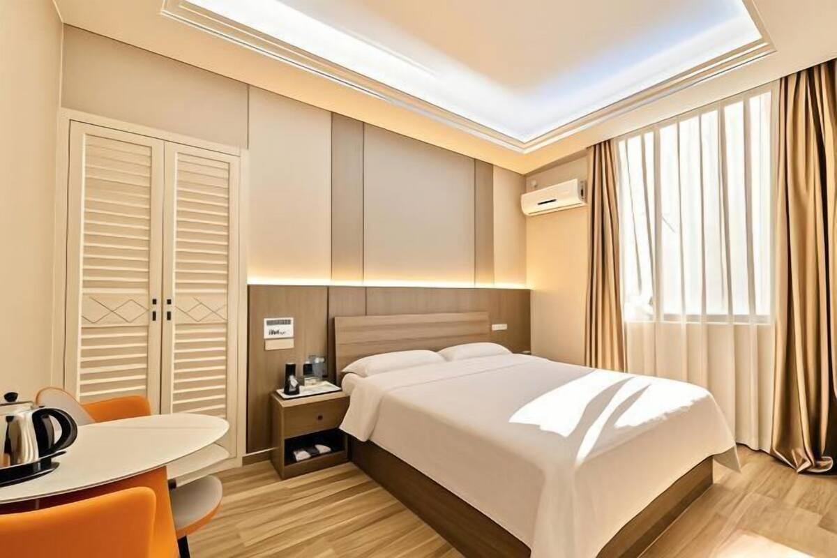 A hotel room with a bed, a desk, a chair, a nightstand, and a wardrobe.