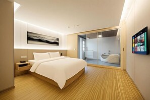 Una habitación de hotel moderna con una cama grande, una mesita de noche, un banco empotrado, un espejo amplio y una puerta corredera que da a un baño con bañera.