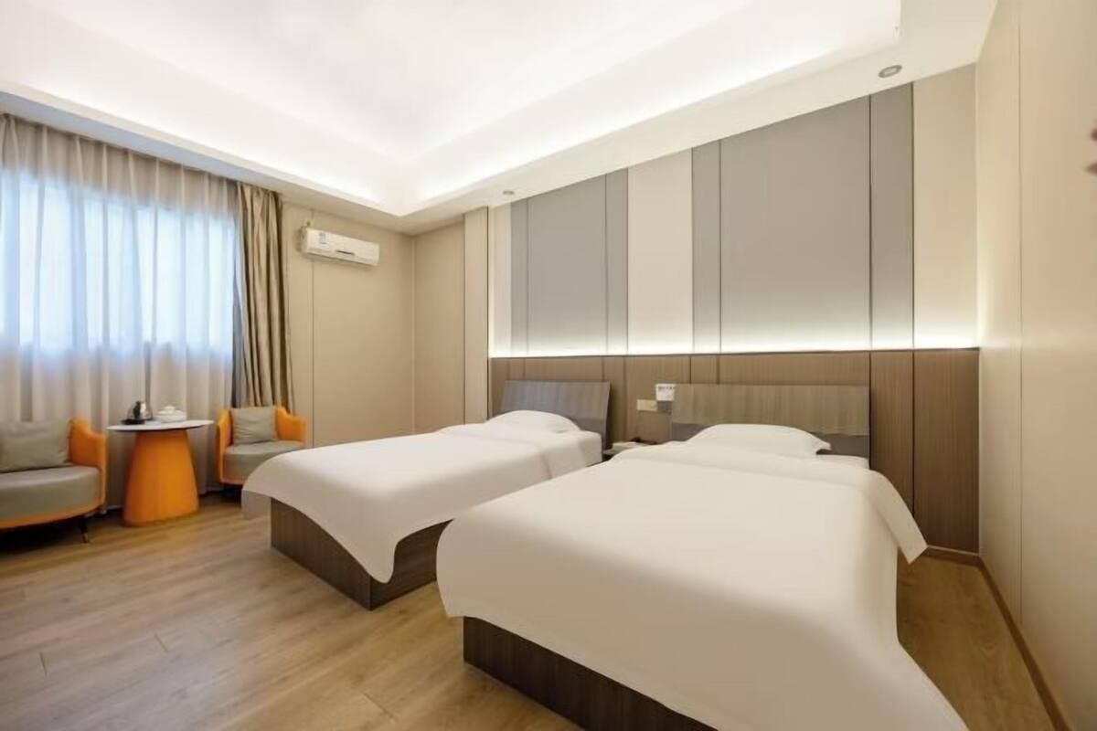 A hotel room with two beds, a sofa, a small table, and a window with curtains.