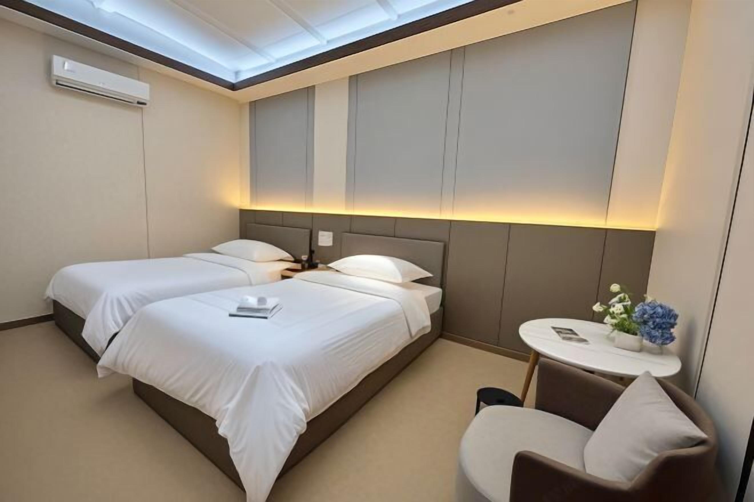 A hotel room with two beds, a small table with a chair, and a skylight above.