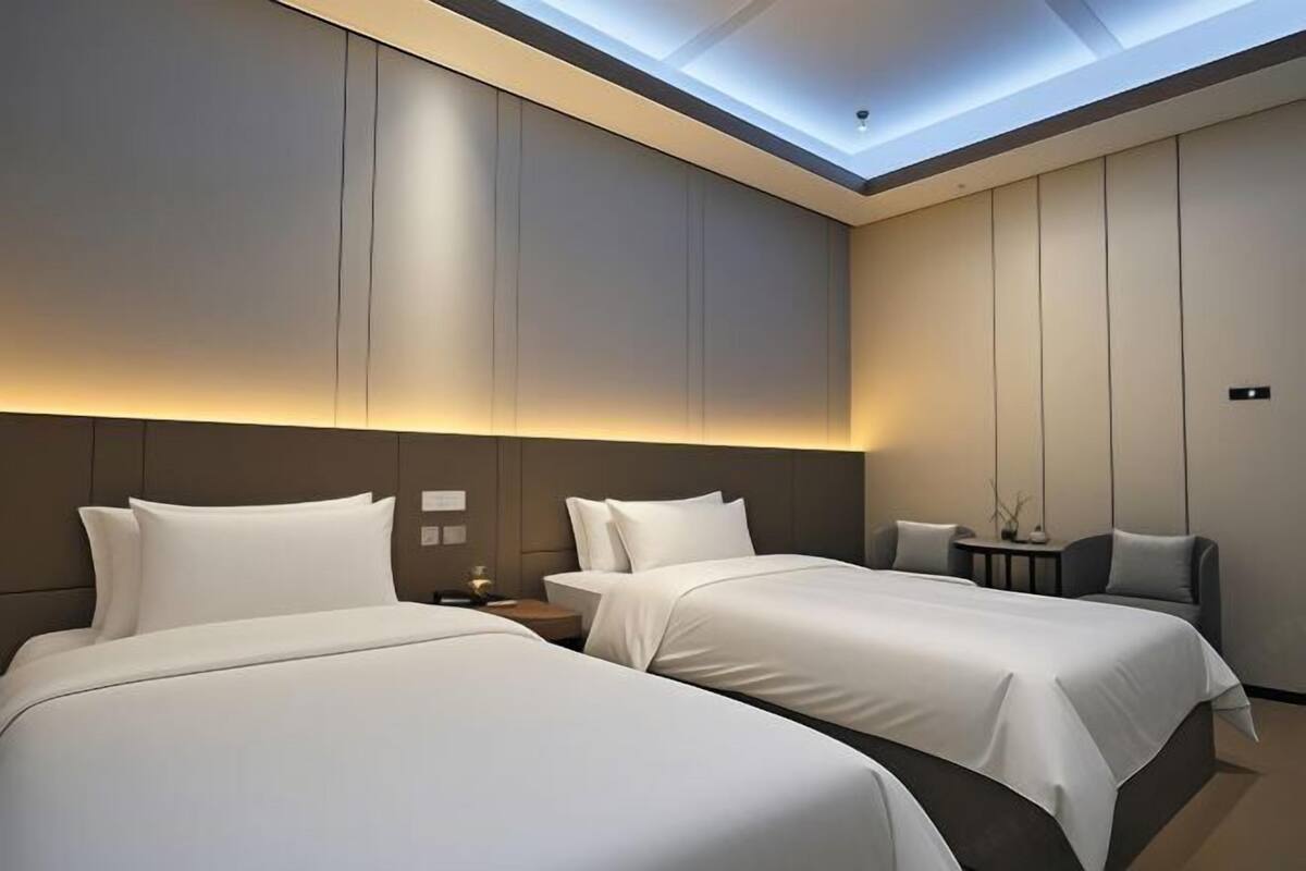 A hotel room with two beds, a small table, and a chair.