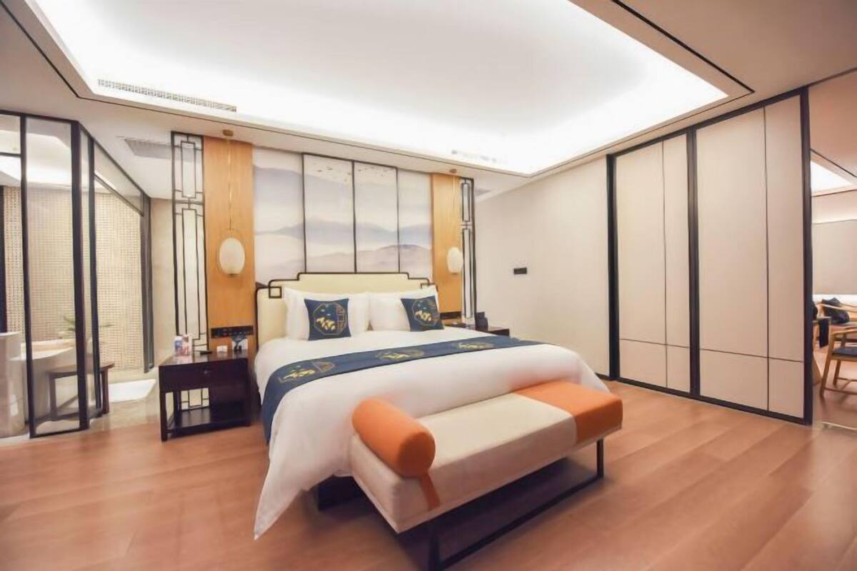 A modern hotel room with a large bed, a bedside table, a desk, and a view of the outdoors.