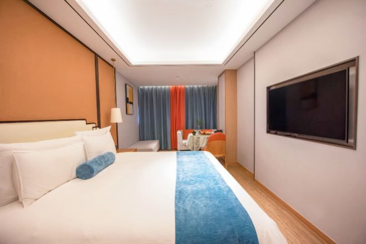 Habitación de hotel con cama, escritorio, silla, televisión y ventana con cortinas.