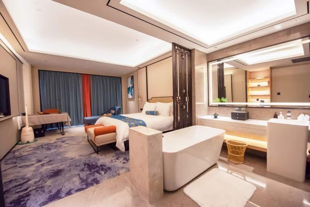 A modern hotel room with a bed, a desk, a bathroom, and a large mirror.