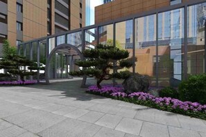 A modern building with a glass facade, a covered entrance, and landscaped areas with trees and flowers. - Shipu Hotel (Ningbo Science and Technology Innovation Center, Wisdom Park) (Ningbo)