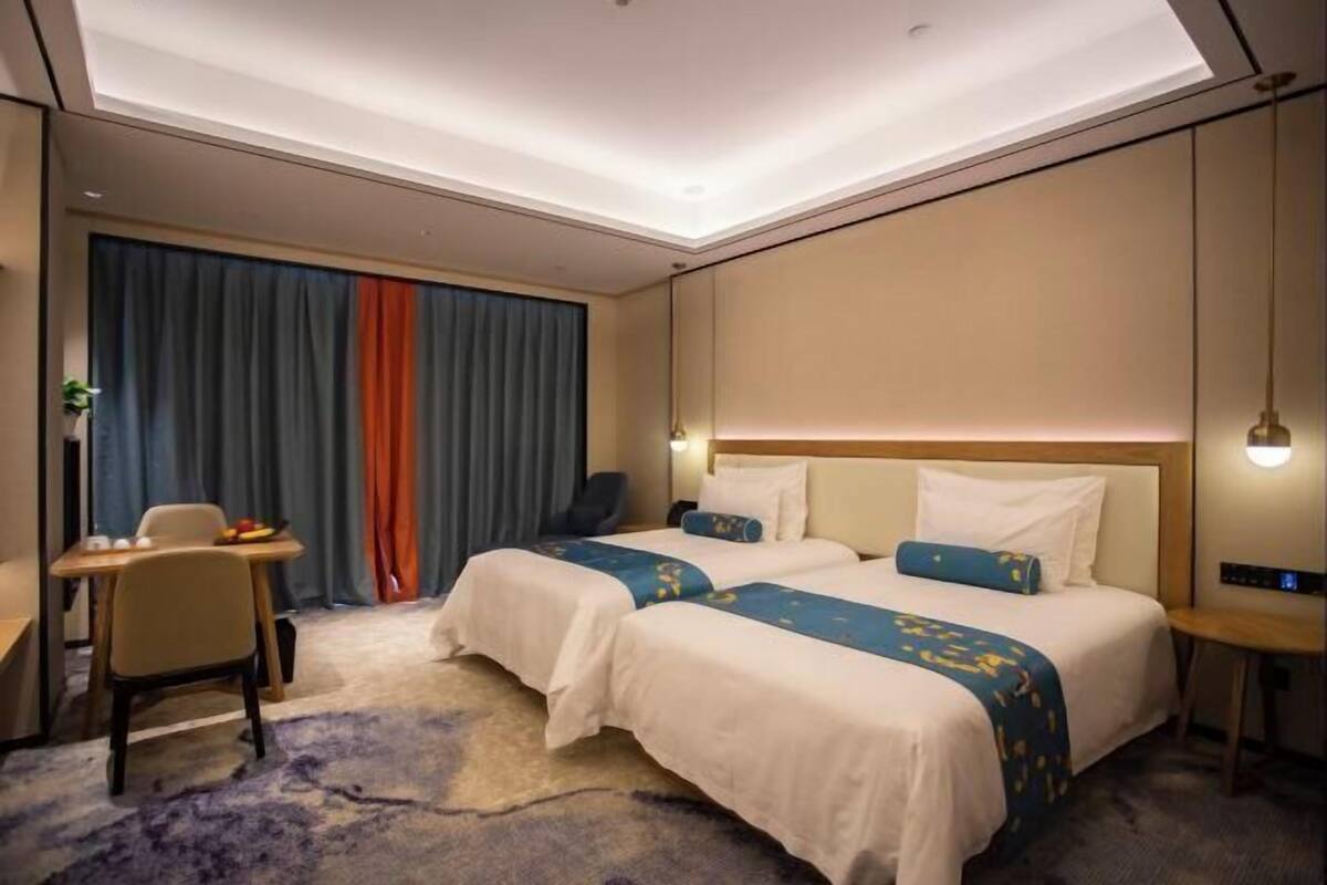 A hotel room with two beds, a desk, a chair, and a large window with curtains.