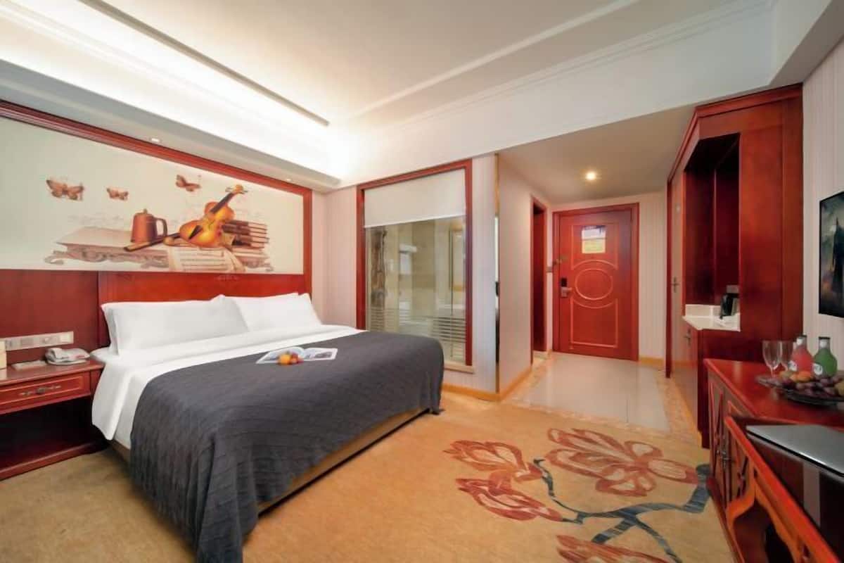 A hotel room with a bed, a desk, a TV, and a door leading to a bathroom.