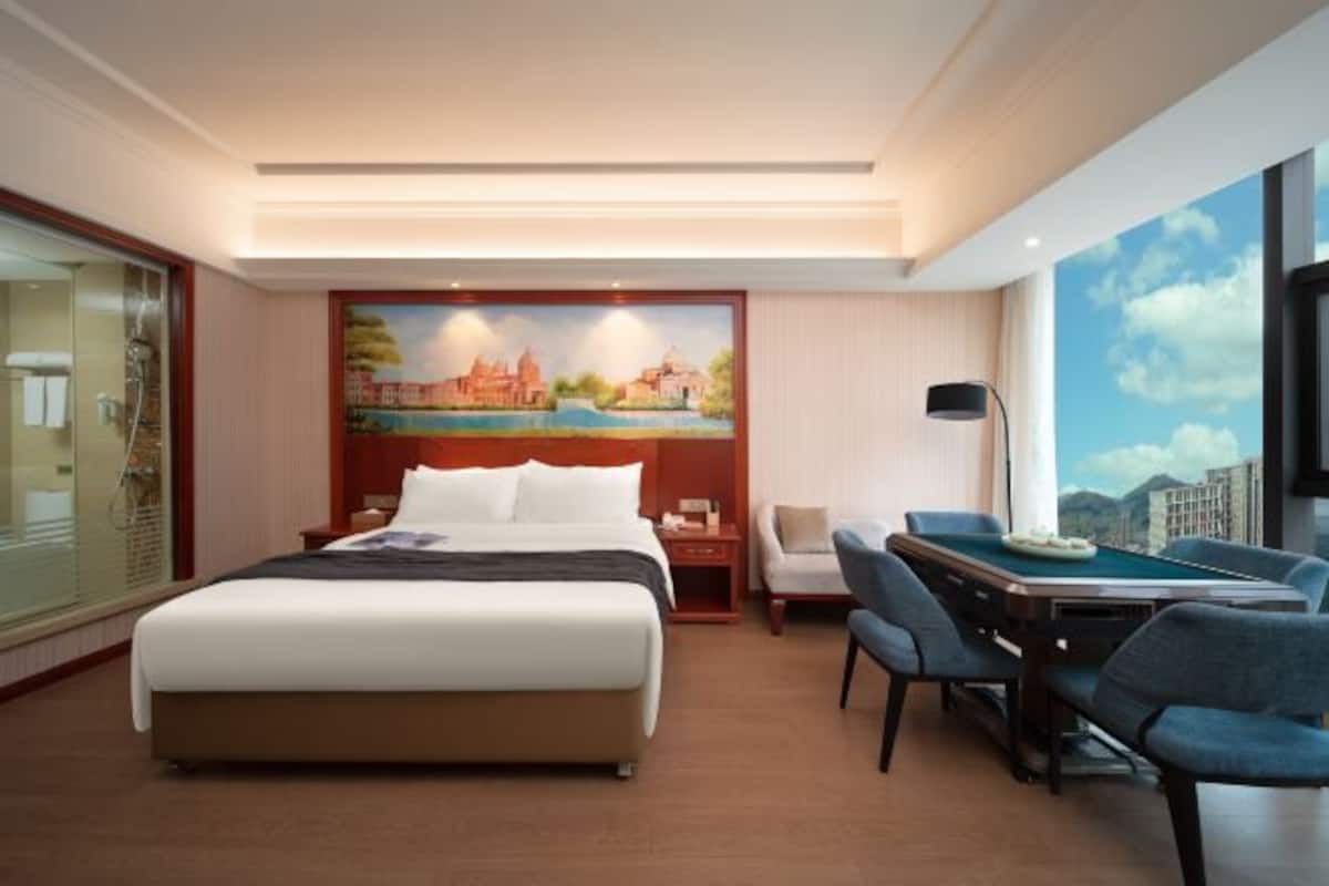A hotel room with a large bed, a desk with a pool table, and a cityscape view.