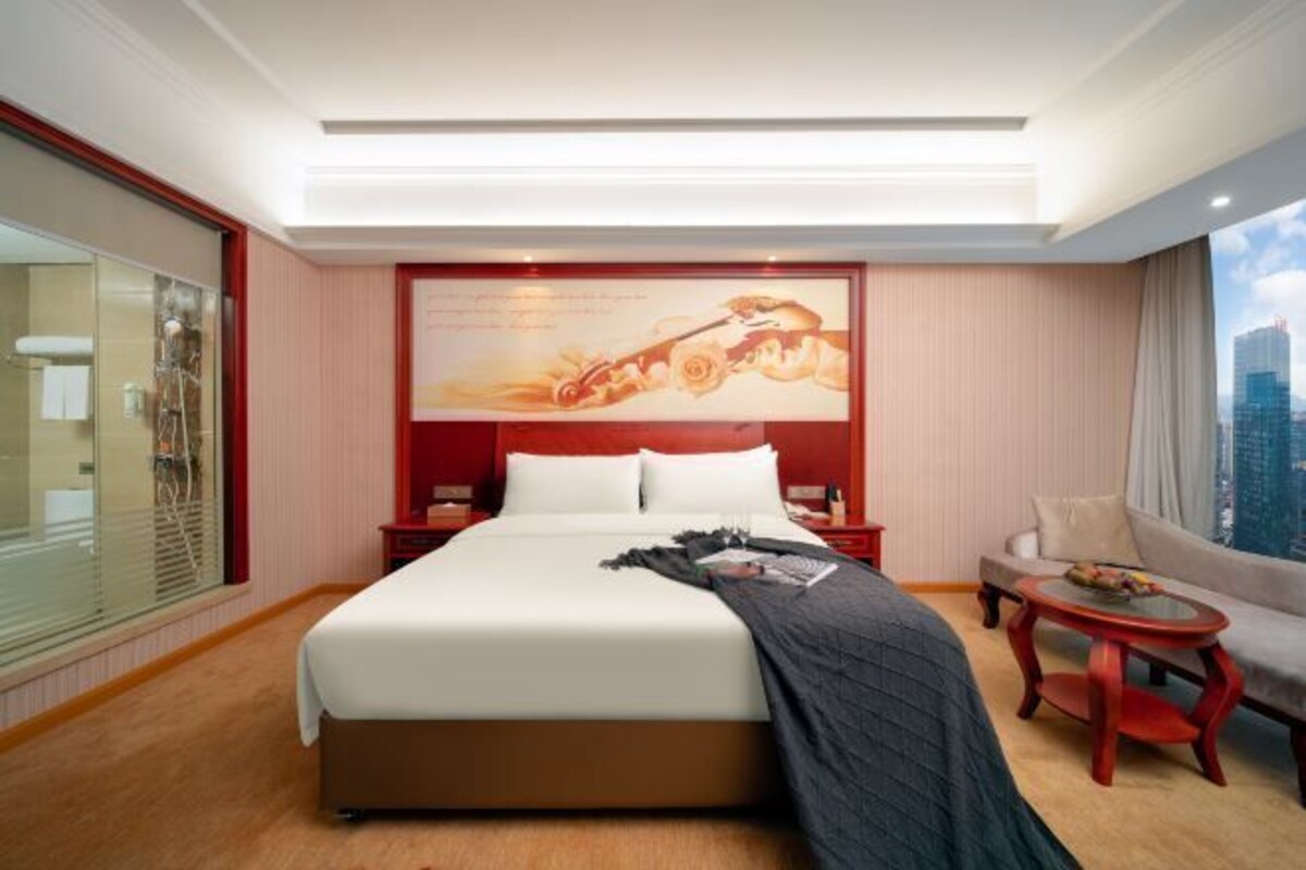 A hotel room with a large bed, a desk, a chair, and a view of the city.