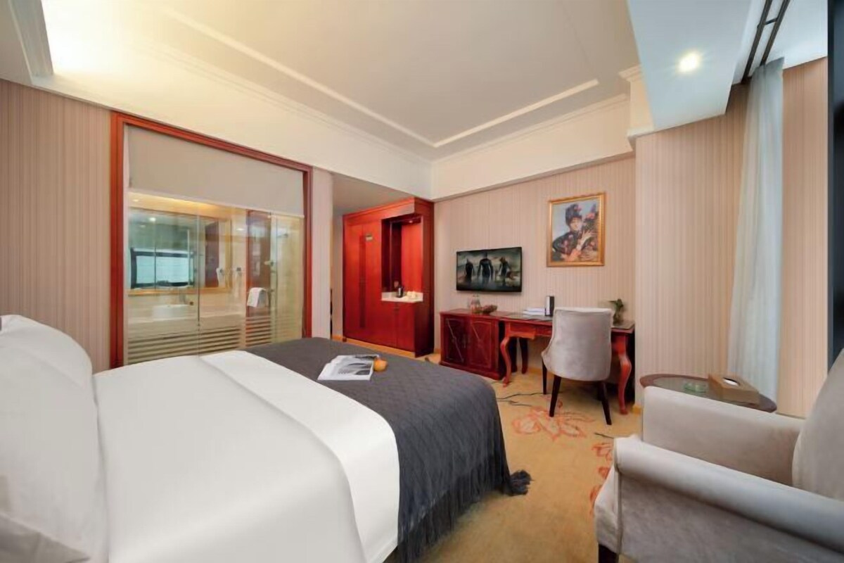 A hotel room with a bed, a desk, a chair, a TV, and a painting on the wall.