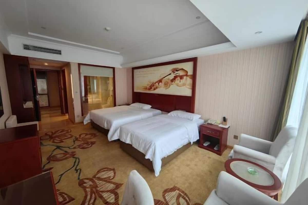 A hotel room with two beds, a desk, a chair, a small table, and a painting on the wall.