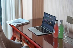 A hotel room with a wooden desk, a laptop, a book, two bottles of water, and a glass.