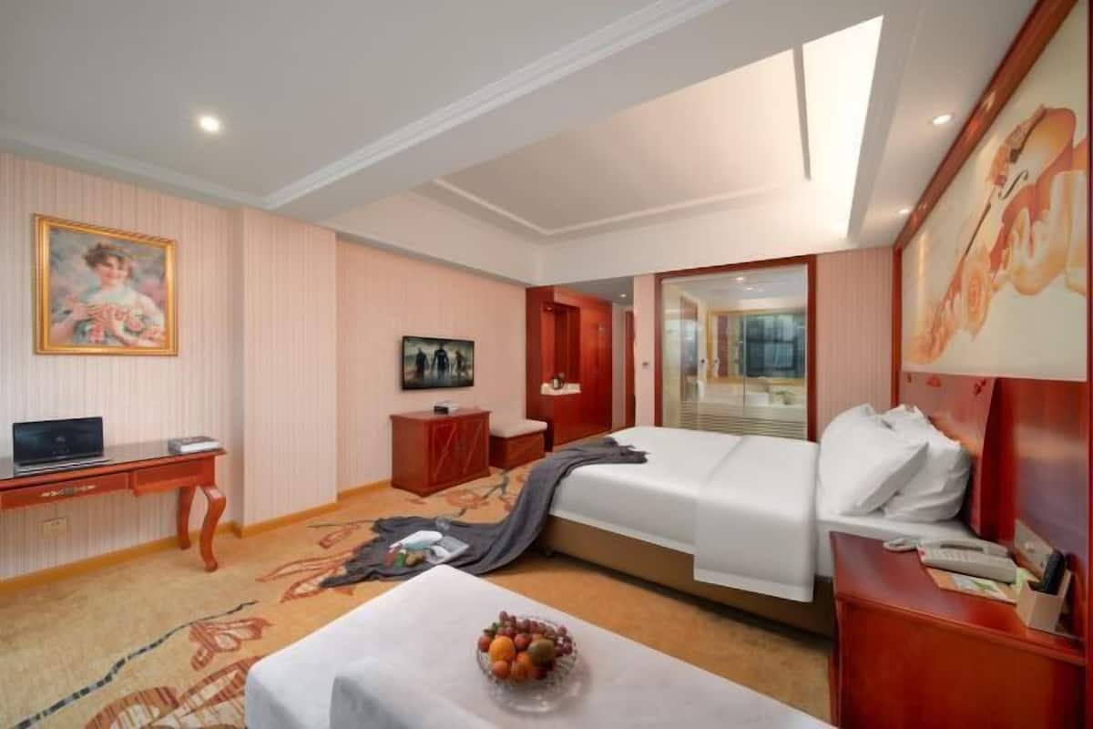 A hotel room with a bed, a desk, a chair, a TV, and a painting on the wall.