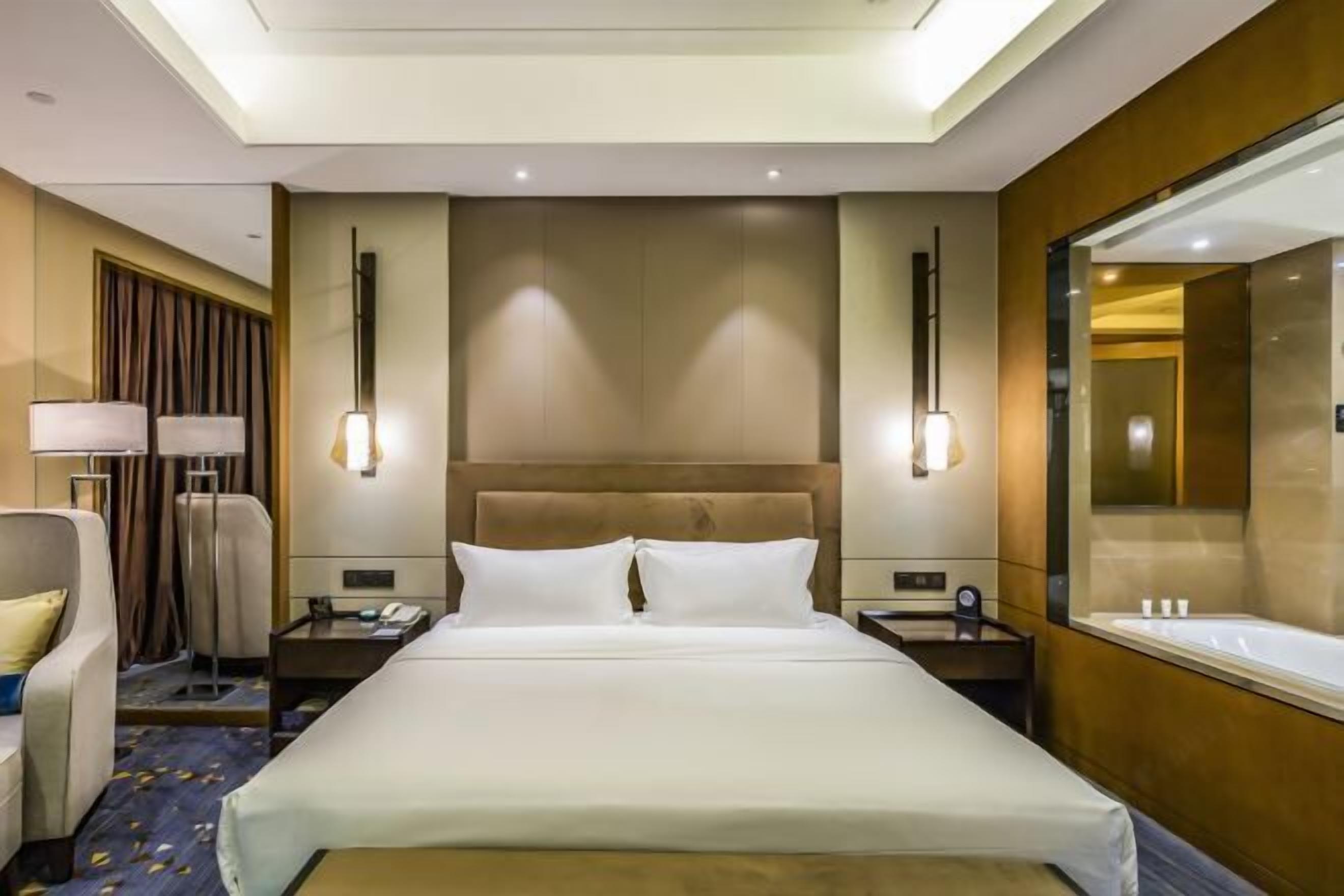 A hotel room with a large bed, bedside tables, a chair, a desk, and a large mirror.