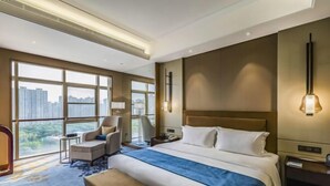 A modern hotel room with a large bed, a desk, a chair, and a view of the cityscape through large windows. - Shangqiu Xinhua Jianguo Hotel (Shangqiu)