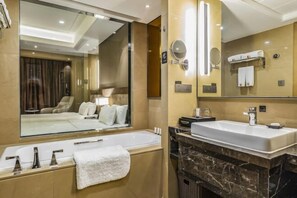 A modern bathroom with a large mirror, a bathtub, a vanity with a sink, and a towel rack.