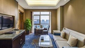 A modern hotel room with a large TV, a sofa, a coffee table, and a balcony with a city view. - Shangqiu Xinhua Jianguo Hotel (Shangqiu)