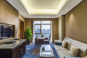A modern hotel room with a large TV, a sofa, a coffee table, and a balcony with a city view. - Shangqiu Xinhua Jianguo Hotel (Shangqiu)