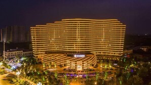 A multi-story hotel with a curved facade, surrounded by a landscaped garden and parking area. - Shangqiu Xinhua Jianguo Hotel (Shangqiu)