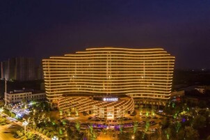Un hotel de varios pisos con fachada curva, rodeado de un jardín ajardinado y zona de estacionamiento.