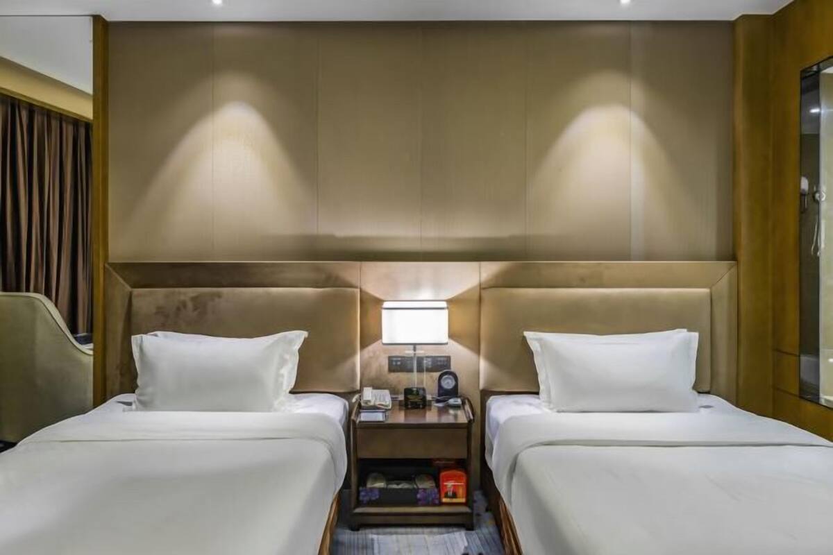A hotel room with two beds, a nightstand with a lamp, and a wooden headboard.