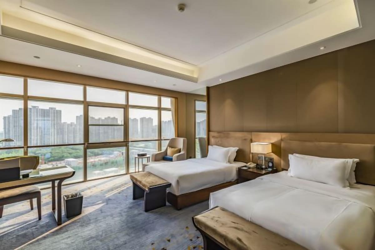 A hotel room with two beds, a desk, and a view of the city.