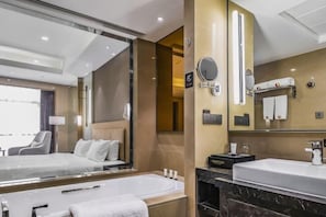 A modern hotel room with a large bed, a separate bathroom with a bathtub, a large mirror, and a view of the outside. - Shangqiu Xinhua Jianguo Hotel (Shangqiu)