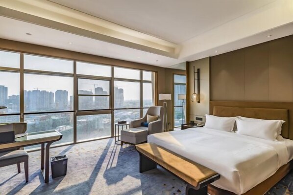 Un moderno cuarto de hotel con una cama grande, un escritorio, una silla y vistas a la ciudad a través de amplias ventanas.