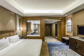 A hotel room with a large bed, a desk, and a mirror. There is a door leading to a bathroom. - Shangqiu Xinhua Jianguo Hotel (Shangqiu)