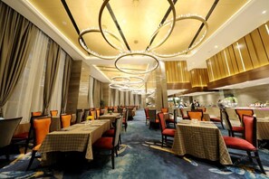 A hotel dining area with multiple tables, chairs, and a modern chandelier.