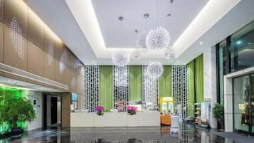A modern hotel lobby with a reception desk, green curtains, and decorative spherical lights.