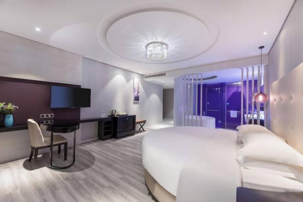 Una habitación de hotel moderna con una cama grande, un escritorio con silla, un televisor y una araña.