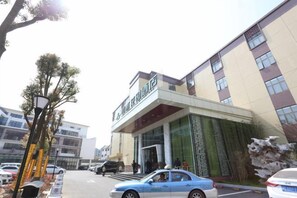 Hotel com fachada moderna, entrada coberta e estacionamento com carros.